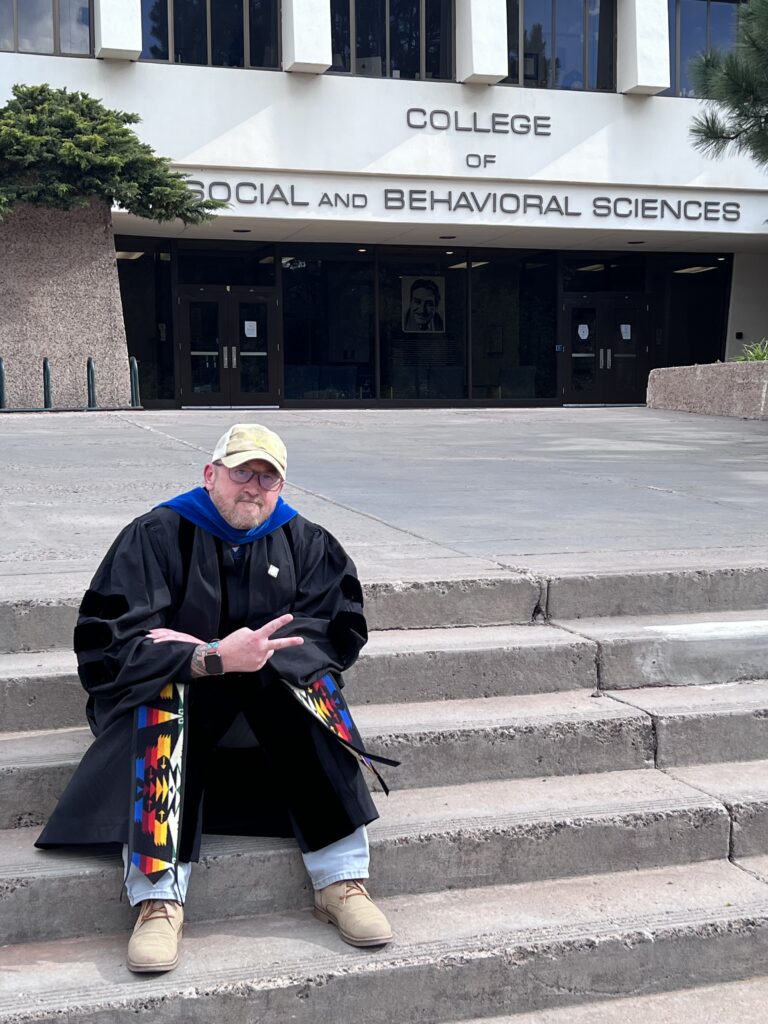 Gavin Healey sitting on stairs dressed in college graduation gown.